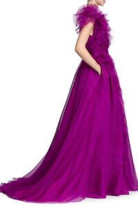 A bridesmaid shows the side of her bridesmaid's dress, 32821 by Marchesa. The stunning purple evening gown has a plunging neckline, a cascading ruffle, and a banded waist. It is available at a boutique in Chicago, IL.