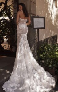 A bride shows the train on the back of her wedding dress, Rania by Eden Aharon. The strapless fit and flare bridal gown features 3D floral appliques. See it at a bridal shop in Chicago, IL.