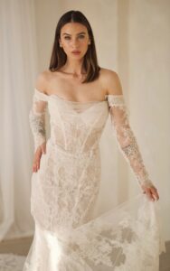 A close-up view of a bride wearing the 1752 wedding dress by Martina Liana. It is a lace bridal gown with a sweetheart neckline and sheer strapless bodice. The fit and flare silhouette dress is shown with the detachable off-the-shoulder long lace sleeves. See it at a bridal shop in Chicago, IL.