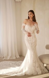 A full-length view of a bride wearing the 1752 wedding dress by Martina Liana. It is a lace bridal gown with a sweetheart neckline and sheer strapless bodice. The fit and flare silhouette dress is shown with the detachable off-the-shoulder long lace sleeves and the dramatic train. See it at a bridal shop in Chicago, IL.