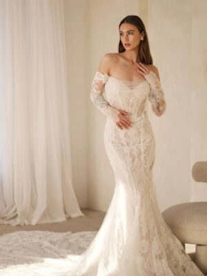 A full-length view of a bride wearing the 1752 wedding dress by Martina Liana. It is a lace bridal gown with a sweetheart neckline and sheer strapless bodice. The fit and flare silhouette dress is shown with the detachable off-the-shoulder long lace sleeves and the dramatic train. See it at a bridal shop in Chicago, IL.