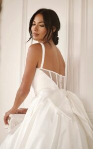 A close-up view of the back of a bride's 1766 wedding dress by Martina Liana. The clean ballgown utilizes high-shine silk fabric and features an oversized detachable bow. This bridal gown is completed with fabric-covered buttons from the waist to the end of the train. Available at a bridal shop in Chicago, IL.