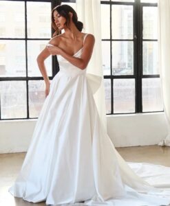 A bride moves the strap of her 1766 wedding dress by Martina Liana. The clean ballgown utilizes high-shine silk fabric and features an oversized detachable bow in the back. This bridal gown is completed with fabric-covered buttons from the waist to the end of the train. See it at a bridal shop in Chicago, IL.