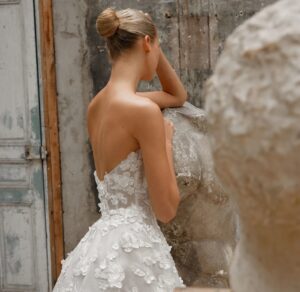 Back details of a strapless gown featuring a sweetheart neckline and a voluminous circle skirt with a dramatic train, crafted from luxurious silk organza and adorned with delicate, handmade flower appliqués