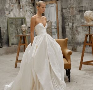 A strapless gown, crafted from luxurious taffeta silk, showcasing a plunging sweetheart neckline and a voluminous hand-draped skirt with a train extension.