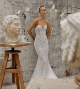 Mermaid gown crafted from a pearl fabric, uniquely designed to layer in intricate formations that flatter the figure, featuring a plunging sweetheart neckline and a train extension.