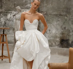 A strapless gown, crafted from luxurious taffeta silk, showcasing a plunging sweetheart neckline and a voluminous hand-draped skirt with a train extension.