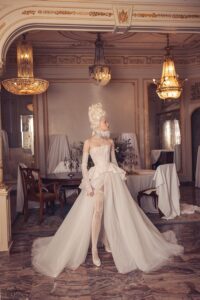 Woman standing in an a-line semi-sheer corset glitter gown with peplum Kim Kassas Victorian collection wedding gown.