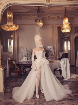 Woman standing in an a-line semi-sheer corset glitter gown with peplum Kim Kassas Victorian collection wedding gown.