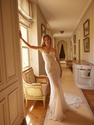 he Calypso gown features a soft peaked sweetheart neckline and a corset bodice, beautifully adorned with dangling beaded freshwater pearls. This fit-and-flare wedding dress showcases a flowing train and an elegant open back.