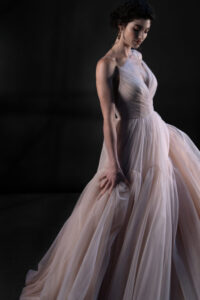 This captivating V-neck gown that whispers romance with its delicate tulle draping, gracefully cascading over the silhouette. The A-line train  trailing behind you as you move,  This enchanting gown is designed to make every moment feel like a fairytale, enveloping you in softness and elegance as you step into your forever.