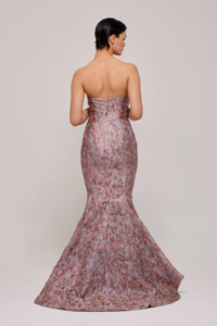 This dazzling multicolored metallic jacquard gown features a strapless bodice that gracefully transitions into a voluminous full skirt. The high-low hem adds a touch of modern elegance, making it the perfect choice for a statement-making look. The intricate jacquard fabric shimmers with a rich array of hues, creating a striking visual effect that captures attention from every angle.