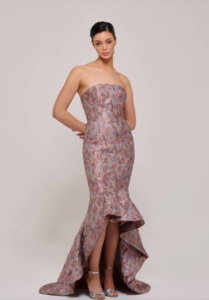 This dazzling multicolored metallic jacquard gown features a strapless bodice that gracefully transitions into a voluminous full skirt. The high-low hem adds a touch of modern elegance, making it the perfect choice for a statement-making look. The intricate jacquard fabric shimmers with a rich array of hues, creating a striking visual effect that captures attention from every angle.