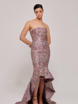 This dazzling multicolored metallic jacquard gown features a strapless bodice that gracefully transitions into a voluminous full skirt. The high-low hem adds a touch of modern elegance, making it the perfect choice for a statement-making look. The intricate jacquard fabric shimmers with a rich array of hues, creating a striking visual effect that captures attention from every angle.