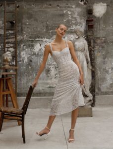 This tea-length evening dress is crafted from shimmering crystal-netted fabric, featuring a straight neckline and delicate shoulder straps for a sophisticated, modern look.