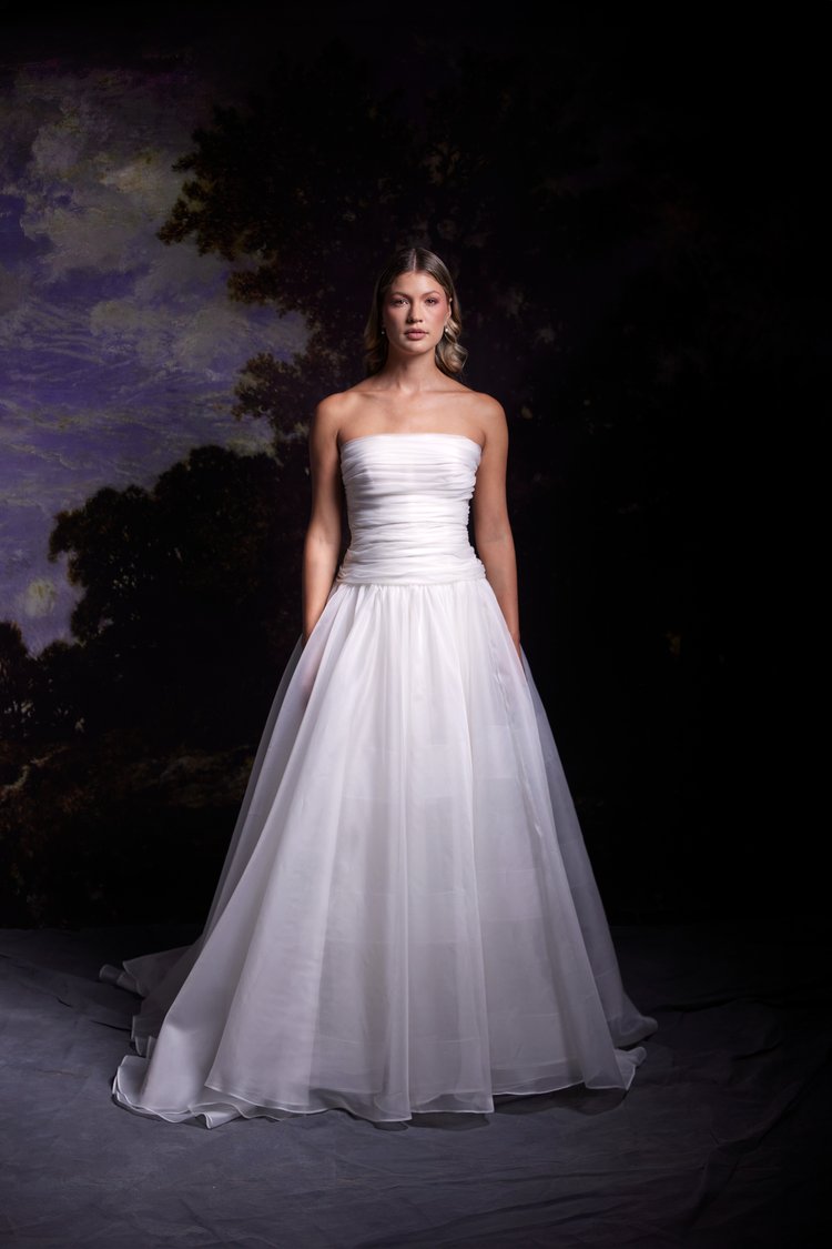 A woman in a wedding dress stands gracefully in front of a large