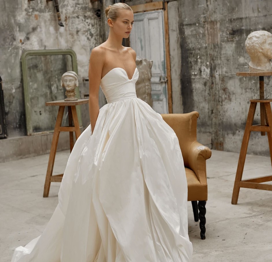 A bride shows the side of her Elle by Dana Harel strapless bridal gown elegantly fashioned from sumptuous taffeta silk that features a daring sweetheart neckline and a beautifully voluminous skirt