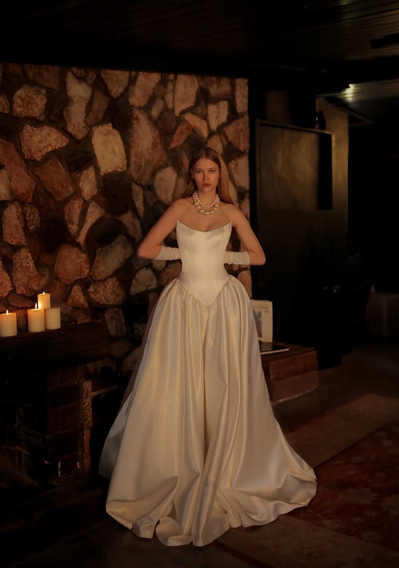 This chic ballgown features a scoop neck and a pointed silky corset with a dropped waist