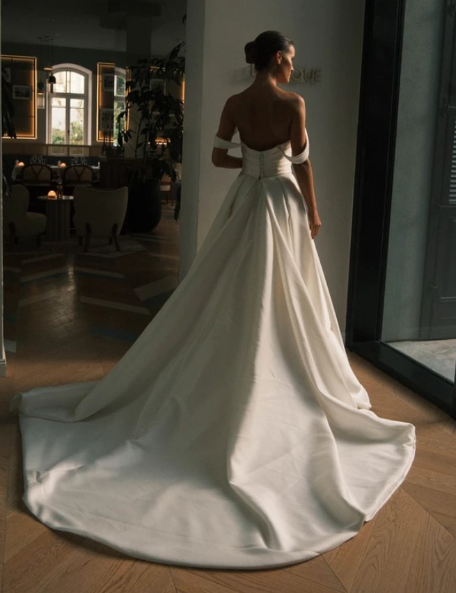 A rear view of a bride showing the dramatic train in the Sydney by Neta Dover wedding dress. This elegant wedding bridal gown features a pleated crossover bodice